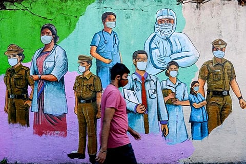 A pedestrian walks past a wall mural featuring illustrations of frontline workers (Credit: AFP)