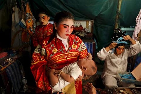 A Chinese opera actress carries her baby backstage before the start of a performance