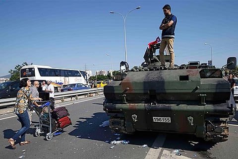 A man looks from atop a military vehicle as a woman passes by, in front of Sabiha Airport
