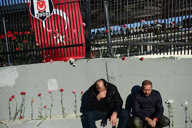 Two men squat next to carnations laid outside the Vodafone Arena football stadium in Istanbul