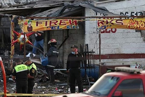 Firefighters and rescue personnel stand near a destroyed house