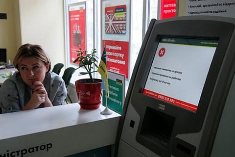 An employee sits next to an out of order payment terminal at Ukraine's state-owned bank Oschadbank