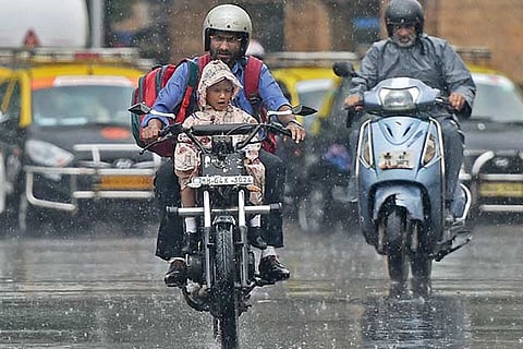 A man carries his child home from school on a motorcycle amid a downpour in Mumbai