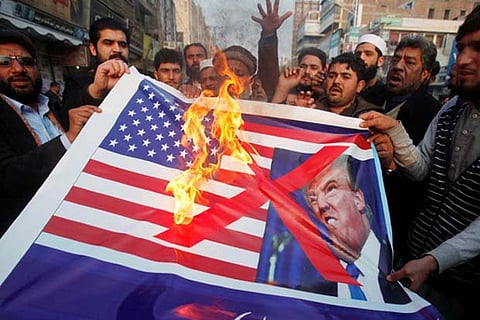 People burn a sign depicting a US flag and a picture of US Prez Donald Trump