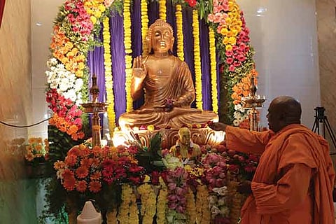 A monk offers flowers to a 6-foot tall Buddha idol. In front of it is a bust of Dr BR Ambedkar