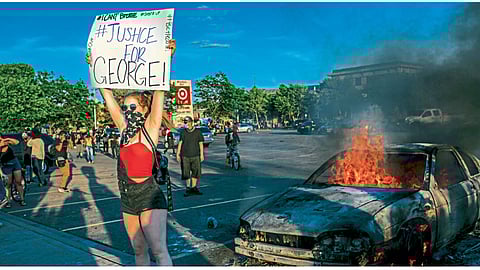 मिनीयापोलिस - जॉर्ज फ्लॉईड मृत्यूप्रकरणी निदर्शकांनी पेटवलेल्या मोटारीपाशी फलक झळकावणारी तरुणी.