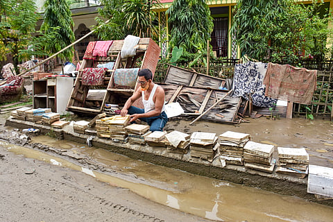 An advocate dries flood-damaged legal books and documents outside his residence after floodwaters receded, in the Santak area of Sivasagar district, Assam, on Monday | PTI