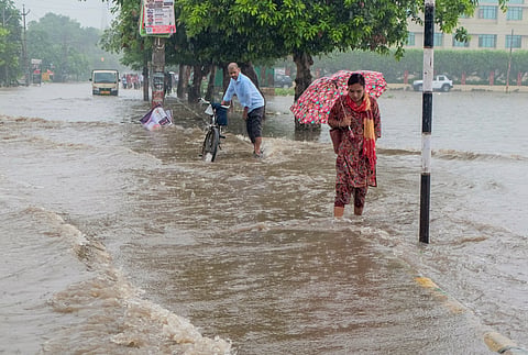 People wade through a waterlogged road amid heavy rain, in Gurugram, on Thursday | PTI