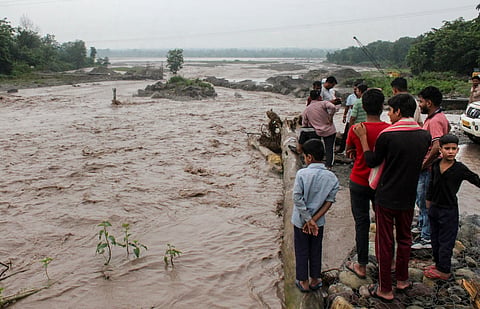 People gather near an overflowing causeway as the swollen Bin river flows following incessant heavy rainfall, in Rishikesh, Uttarakhand, on Tuesday | PTI