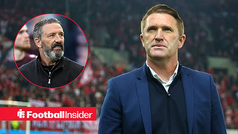 Robbie Keane stood in a suit looking upwards on the sidelines with Derek McInnes left inset looking at him smiling