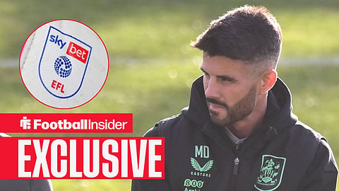 Football Insider exclusive as Huddersfield manager Martin Drury stares towards the EFL badge, which features in a circular inset.