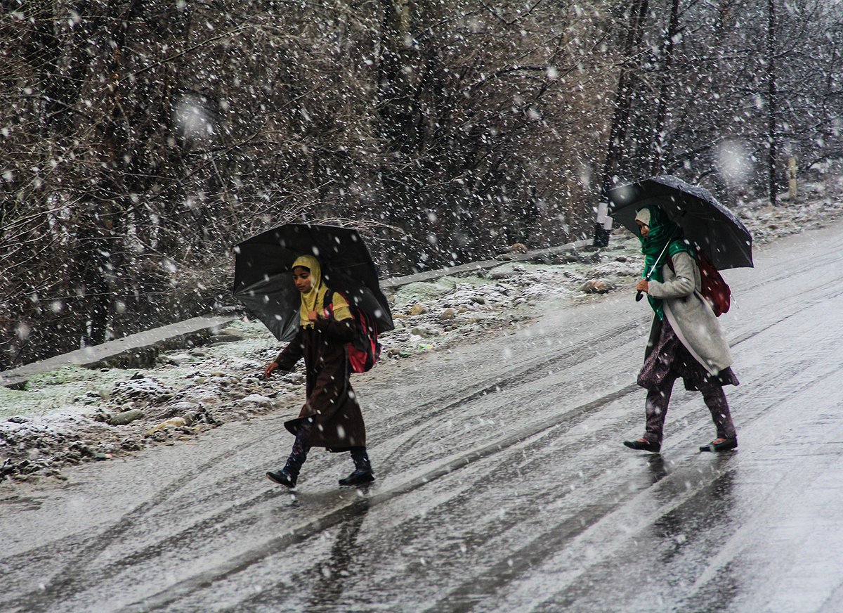 Young girls walk with umbrellas during fresh snowfall in part of Kashmir.