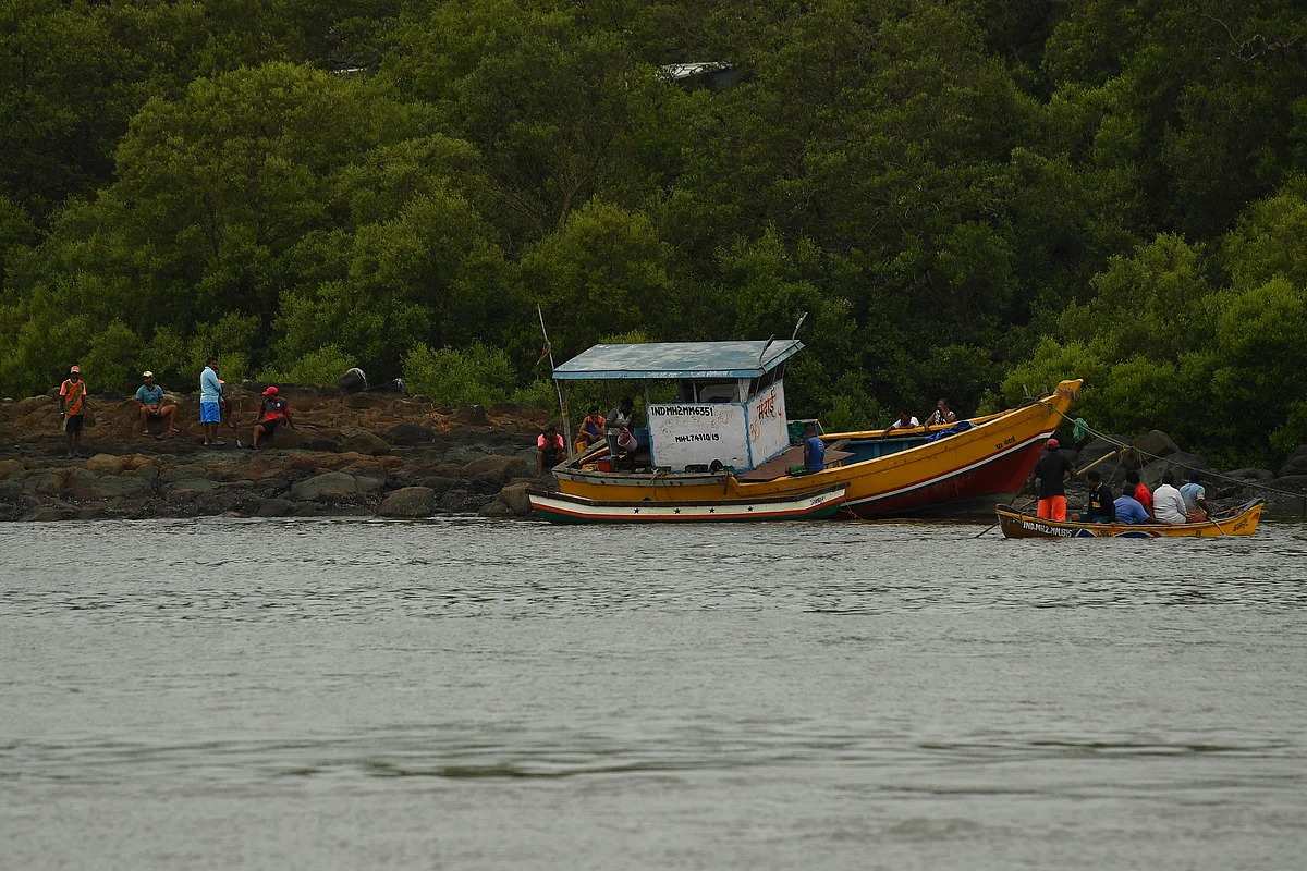 Fishermen are seen next to a fishing dhow that was thrown onto the rocks by strong winds caused by the impending cyclone Tauktae at a fishing village off the city coast in Mumbai on May 16, 2021.