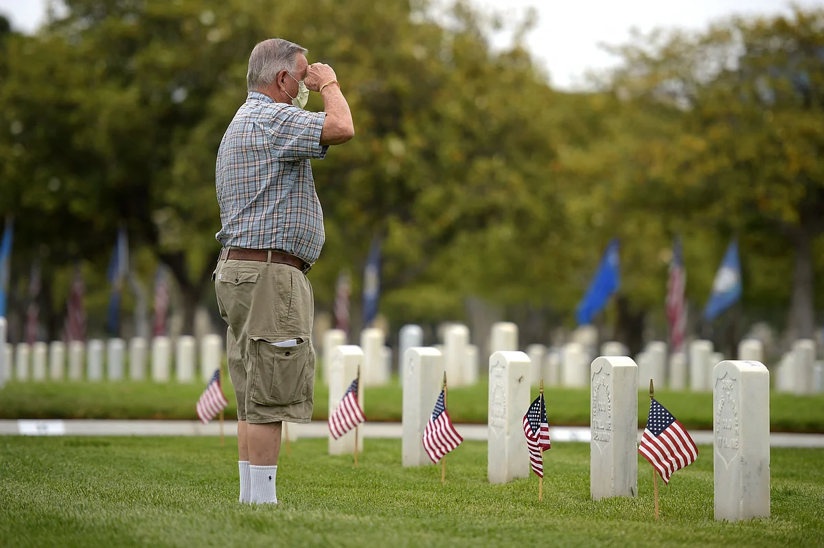 Roy Atherton salutes as he places American flags at graves ahead of Memorial Day in the Los Angeles National Cemetery in Los Angeles, California on May 29, 2021.