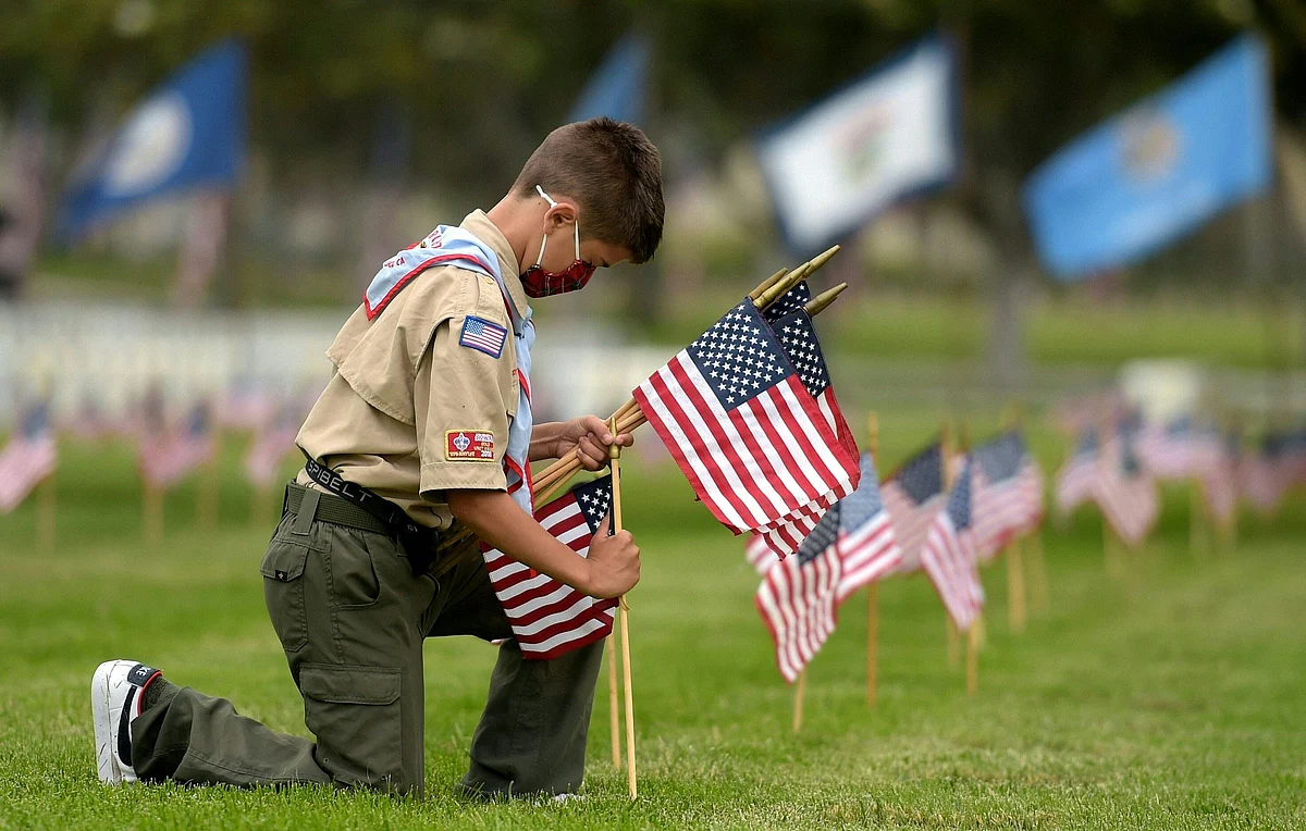 A boy scout places miniature American flags at graves ahead of Memorial Day in the Los Angeles National Cemetery in Los Angeles, California on May 29, 2021.