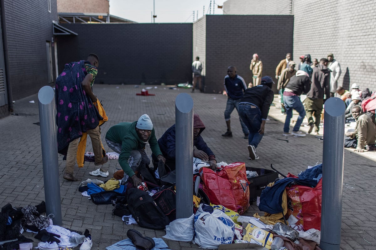 A man detaining for looting tries to hide a six-pack of beers in a bag while gathering with other people suspected of looting in a mall in Vosloorus, on July 13, 2021.