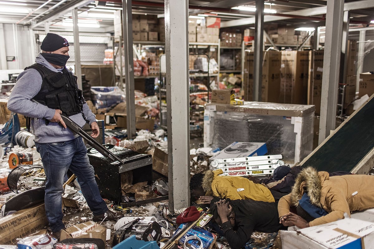 Suspected looters are pinned to the ground by an armed private security officer looking for looters, inside a flooded mall in Vosloorus, on July 13, 2021.