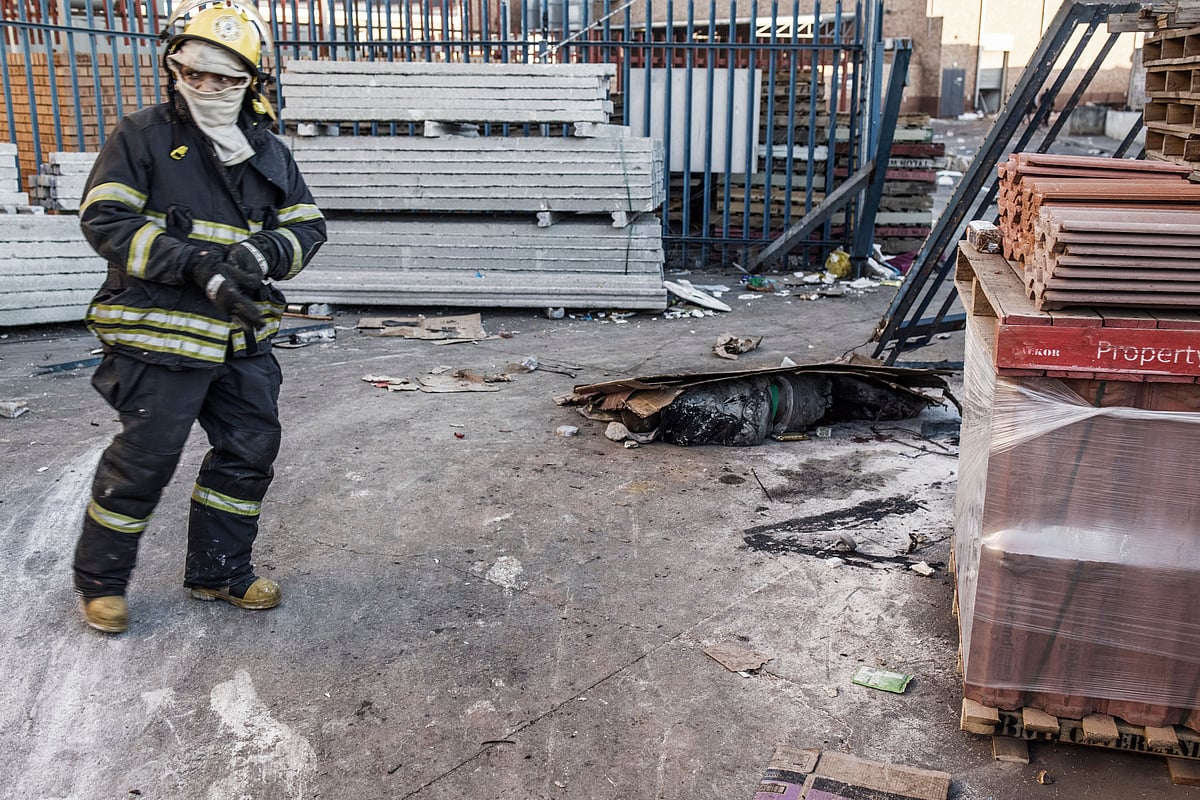 A South African firefighter (L) motions towards the body of a man believed to have been killed overnight at the scene of a looted mall in Vosloorus on the outskirts of Johannesburg on July 14, 2021.