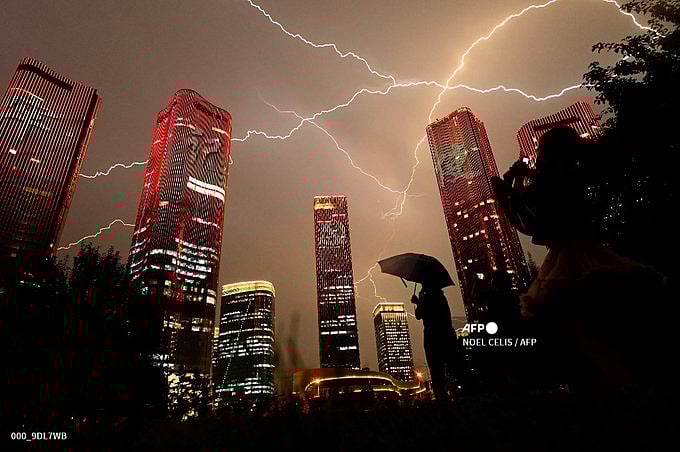 People look at buildings displaying a light show on the eve of the 100th anniversary of the Chinese Communist Party in Beijing on July 1, 2021.