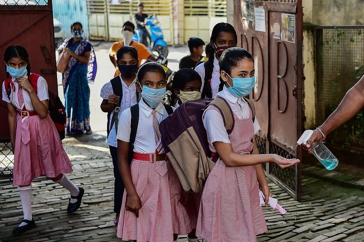 A staff helps students with hand sanitisers as they arrive at a school in Allahabad on September 1, 2021 after the state government relaxed the Covid-19 coronavirus lockdown norms for educational institutions, allowing students from 1st-5th standard to attend physical classes with 50 percent capacity and following all safety protocols against the pandemic.