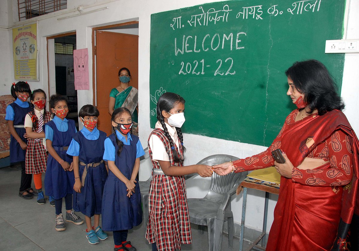 Teacher distributes chocolate to student on their arrival at school in Bhopal on Monday