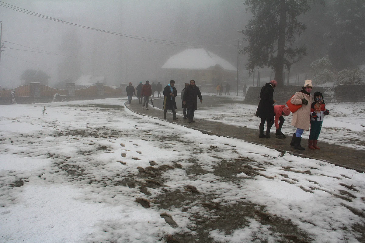 Tourists walk on a road covered with snow during the season's first snowfall, in World famous Ski resort Gulmarg, Kashmir, on October 23, 2021