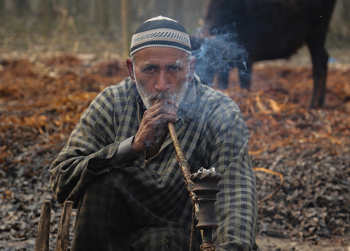 A villager smokes a hubble-bubble pipe as he takes a break from peeling the cover of wicker sticks on the outskirts of Srinagar, Jammu and Kashmir.