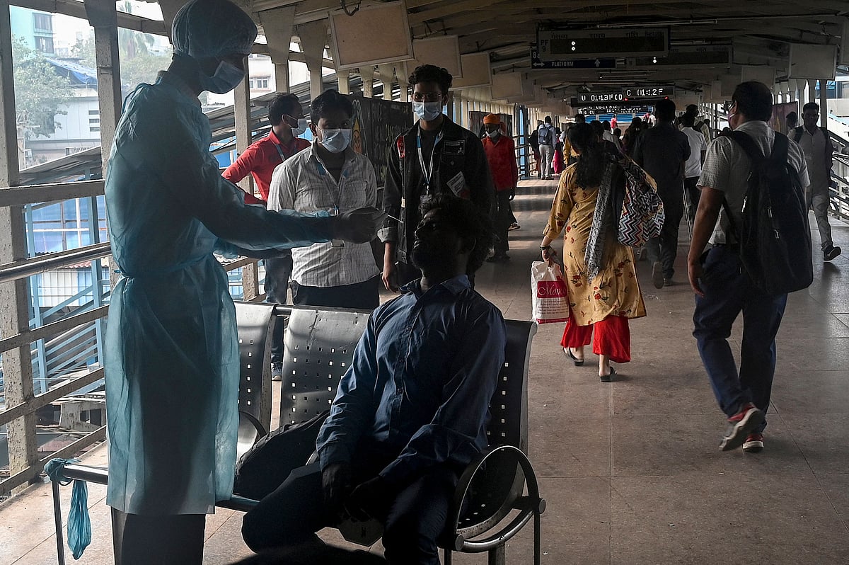 A health worker wearing Personal Protective Equipment (PPE) suit collects a swab sample for RAT (Rapid Antigen Test) of an arriving passenger at a railway station in Mumbai on January 13, 2022.  | (Photo by INDRANIL MUKHERJEE / AFP)