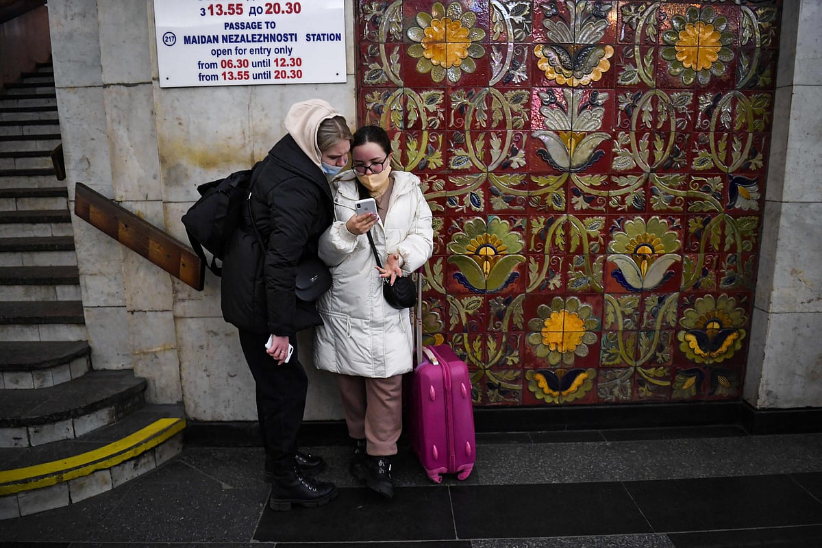 Two young women with a suitcase use a smartphone at a metro station in Kyiv early on February 24, 2022.