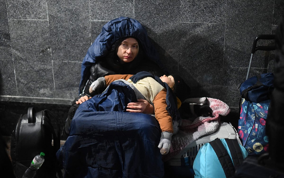 A woman holds her sleeping child while sitting on the ground at Lviv central train station in Western Ukraine on February 26, 2022. | (Photo by Daniel LEAL / AFP)