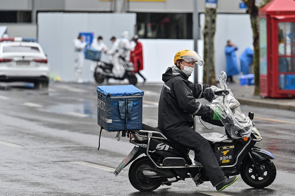 A delivery man rides a scooter to deliver an order next to a locked down neighbourhood after the detection of new cases of Covid-19 in Huangpu district, in Shanghai on March 17, 2022.