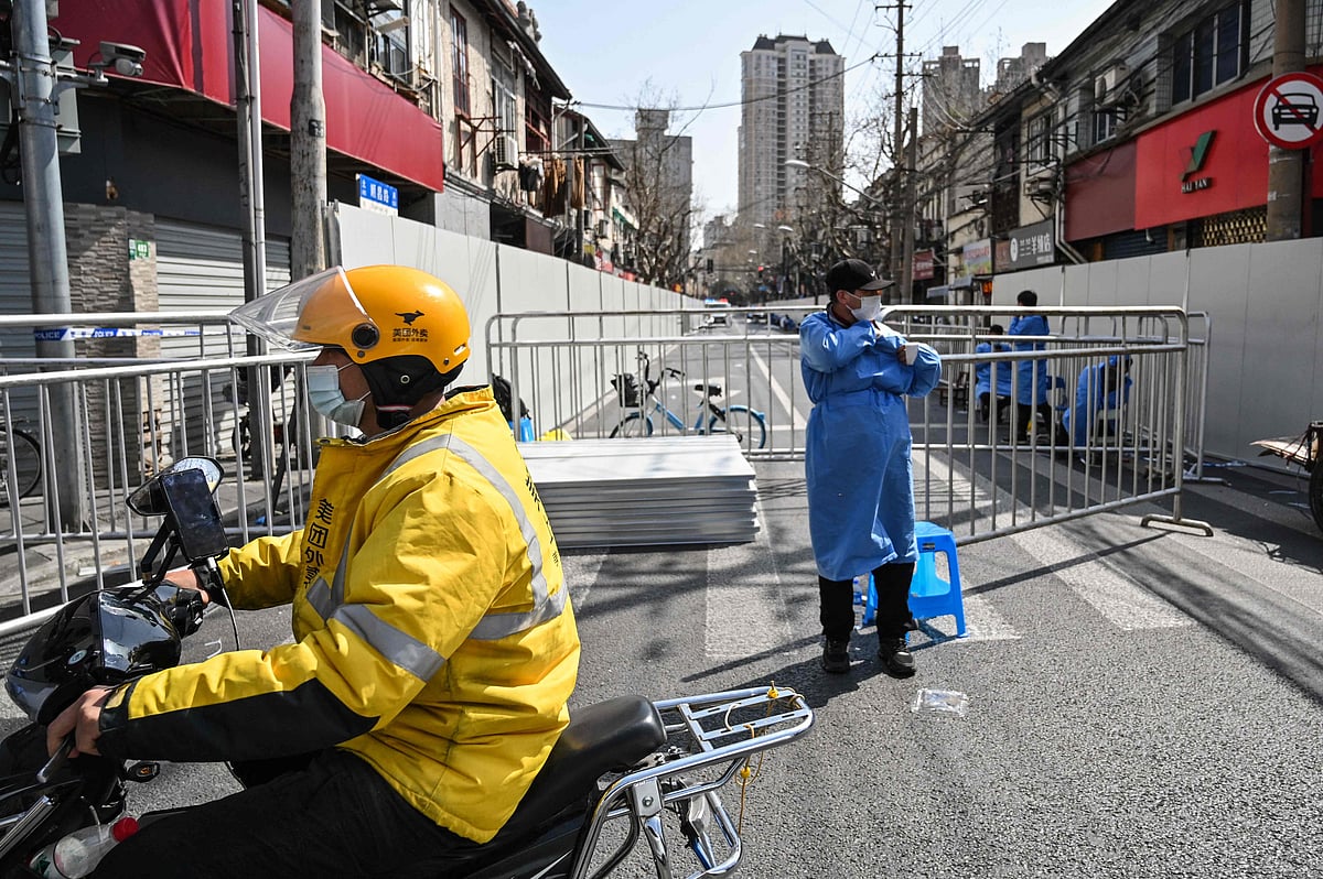 A delivery man (L) rides a scooter next to a locked down neighbourhood after the detection of new cases of Covid-19 in Huangpu district, in Shanghai on March 15, 2022.
