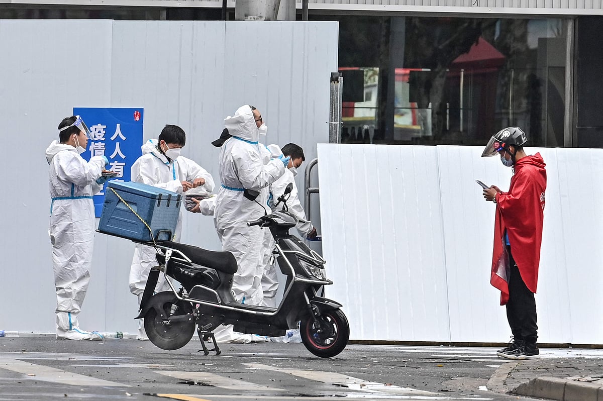 A delivery man (R) is seen next to workers wearing protective gear outside of a locked down neighbourhood after the detection of new cases of Covid-19 in Huangpu district, in Shanghai on March 17, 2022.