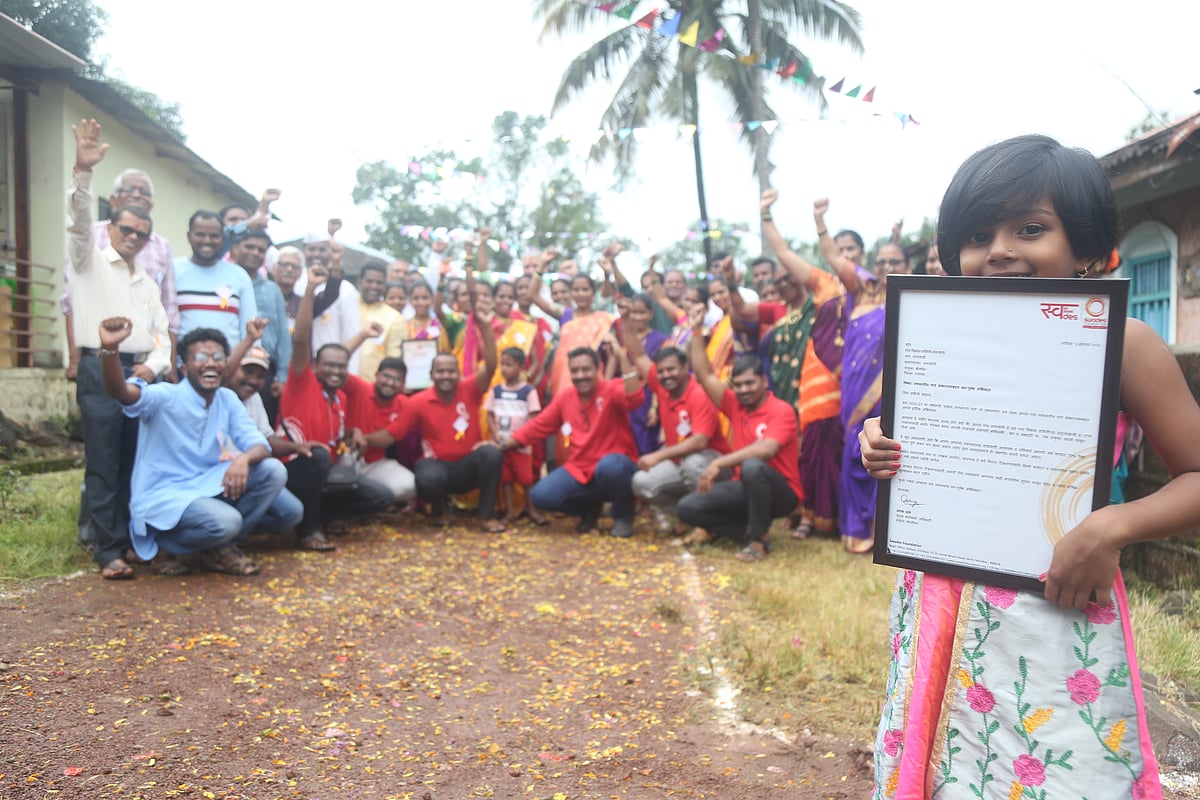 A little girl holds up the Swades Dream Village certificate in Nagloli, Raigad