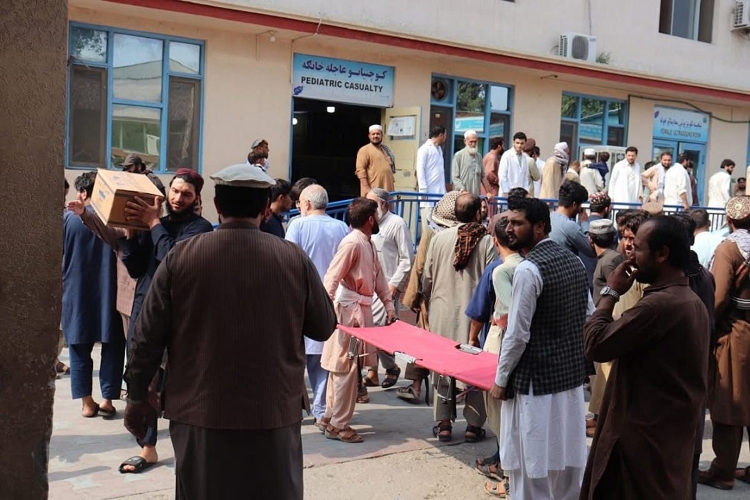Crowds gather outside a paediatric casualty ward in Jalalabad, with locals carrying relief supplies and stretchers.