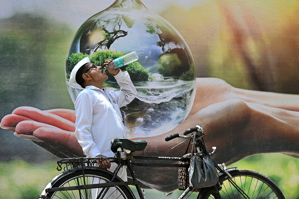 A dabbawala pauses to sip water in front of a mural on World Water Day