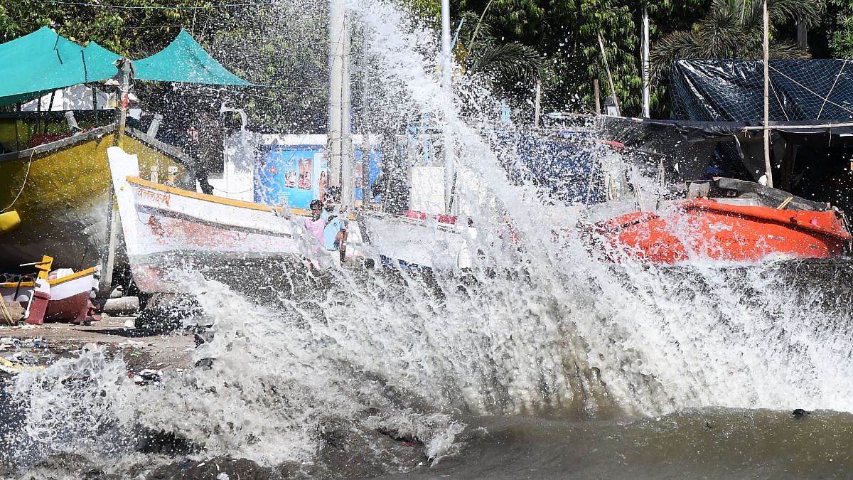 Fishermen stand near their boats as high tidal waves crash onto the shore at
Budhwar Park