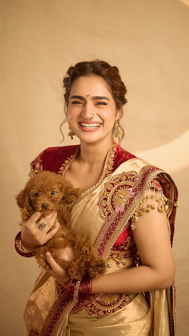 She paired the saree with a deep red blouse that instantly elevated the ensemble. Designed with a V-shaped neckline and a bold open back, it featured ornate gold embroidery across the bodice and sleeves

