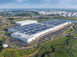 Solar panels on a factory rooftop in the US next to a fossil fuel storage facility. The US solar industry has installed enough capacity to power more than 50 million homes despite new tariffs, permitting barriers and policy uncertainty.