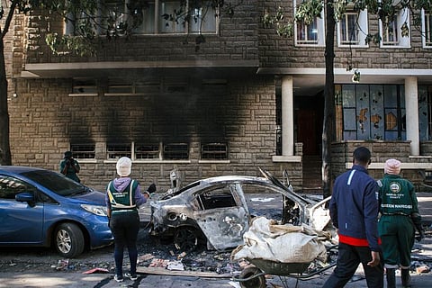 City cleaners look at a burnt-out vehicle following anti-government protests in the Central Business District in Nairobi, Kenya, on Wednesday, June 26, 2024.  
