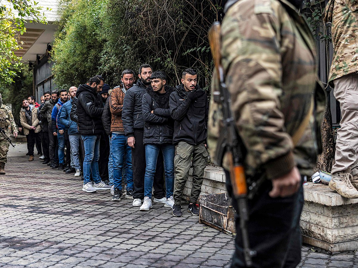 A member of Syria's transitional government security forces stands guard as former soldiers, police members, and civilians queue up at a centre for handing over small arms and security registration with the new authorities in Damascus on December 24, 2024. 
