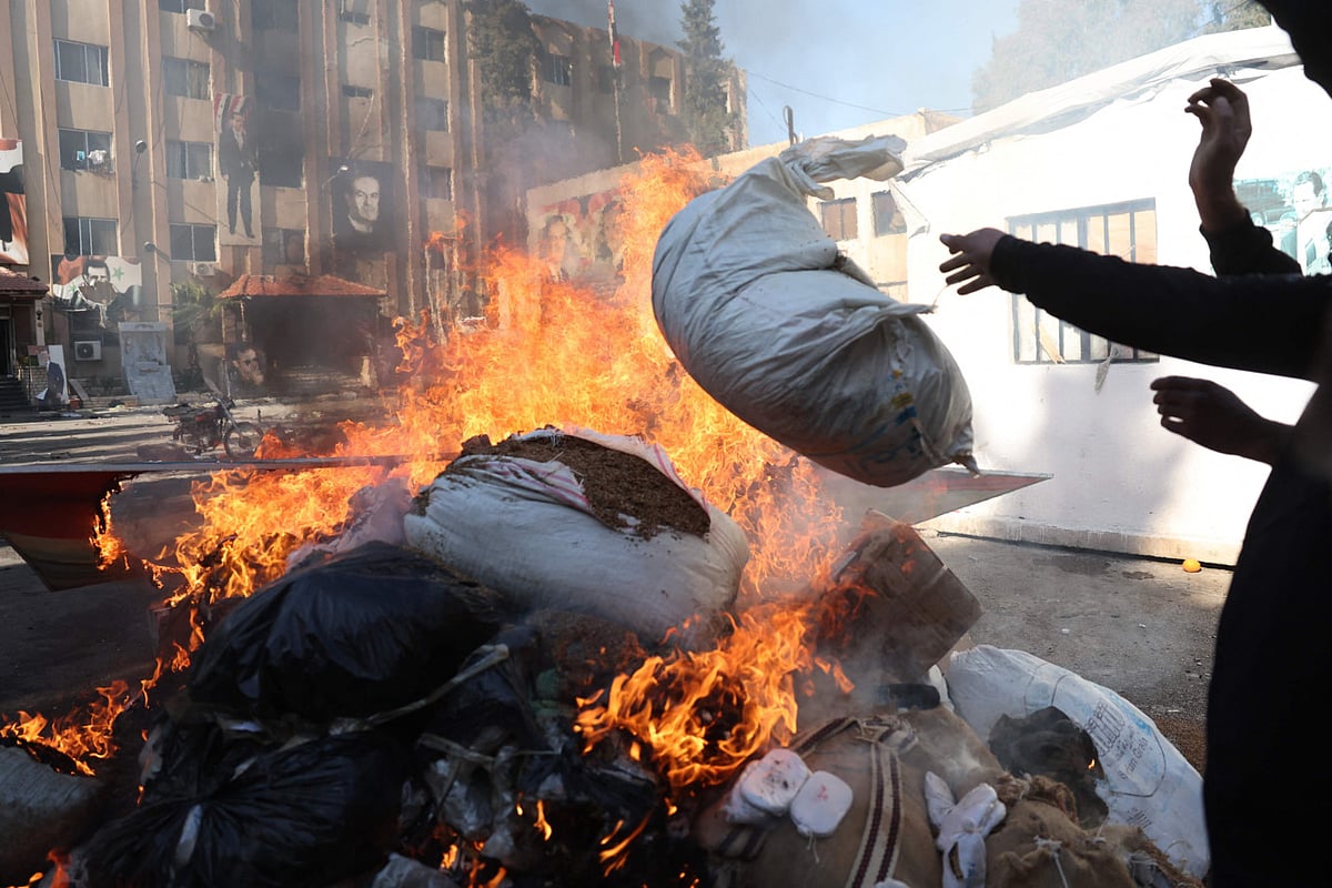 A man throws a bag onto a pile of burning illicit drugs, as Syria's new authorities burn drugs reportedly seized from a security branch, in Damascus on December 25, 2024.  