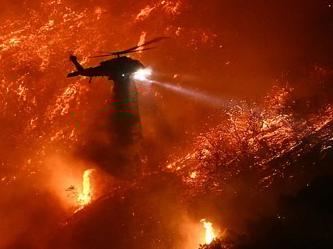 A fire fighting helicopter drops water as the Palisades fire grows near the Mandeville Canyon neighborhood and Encino, California.
