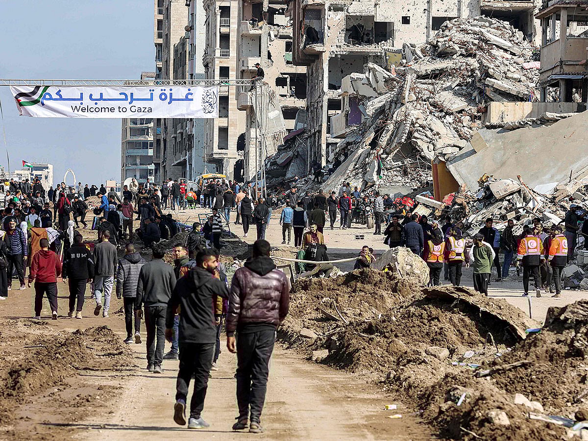 People gather by a banner welcoming people near the rubble of a collapsed building along Gaza's coastal Al Rashid Street for people to cross from the Israeli-blocked Netzarim corridor from the southern Gaza Strip into Gaza City.
