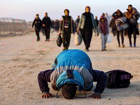 A boy prostrates in a prayer of gratitude as people walk along Gaza's coastal Al Rashid Street to cross the Netzarim corridor from the southern Gaza Strip into the north.