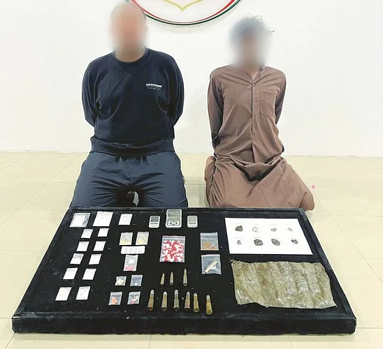 Two suspected drug dealers in Kuwait appear in a police photo with illicit substances seized in their possession.