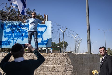 An Israeli right wing activist waves a national flag as he poses in front of the defaced sign board at the shuttered gate of the United Nations Relief and Works Agency on January 30, 2025.