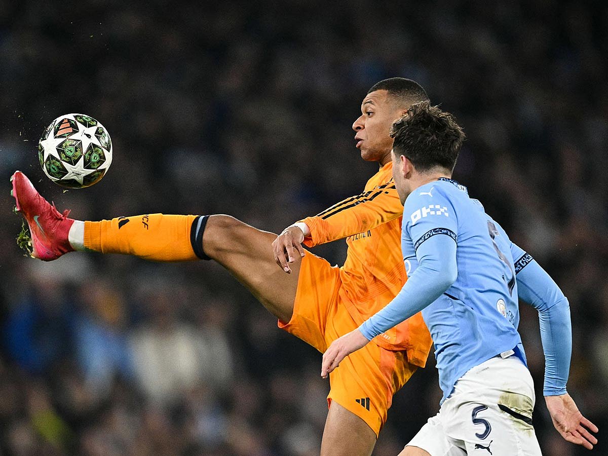 Real Madrid's Kylian Mbappe (rear) controls the ball past Manchester City's John Stones during the UEFA Champions League football match at the Etihad Stadium in Manchester, north west England, on February 11, 2025.