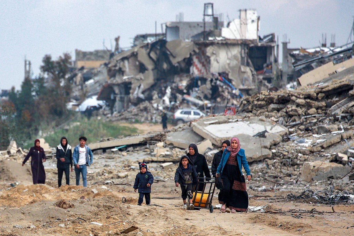 Women and children walk along a destroyed road past collapsed buildings in the west of Beit Lahia in the northern Gaza Strip amid the current ceasefire deal in the war between Israel and Hamas.