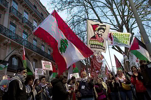 A protester holds the Lebanese flag and a flag that reads in French, "Free Georges Abdallah" during a rally to demand the release of Lebanese pro-Palestinian activist Georges Ibrahim Abdallah, in prison for some 40 years, in Toulouse on February 19, 2025.